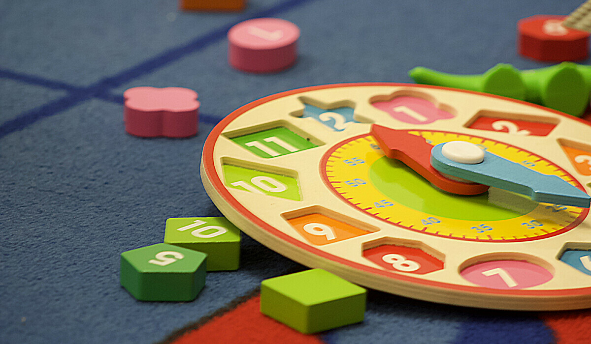 Colourful wooden clock toy with scattered number pieces on a blue carpet.