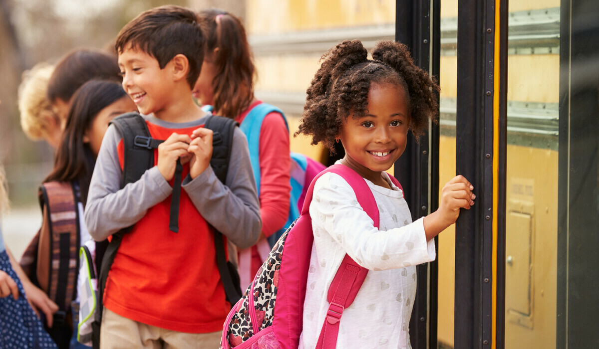 Children boarding a school bus, one smiling at the camera.