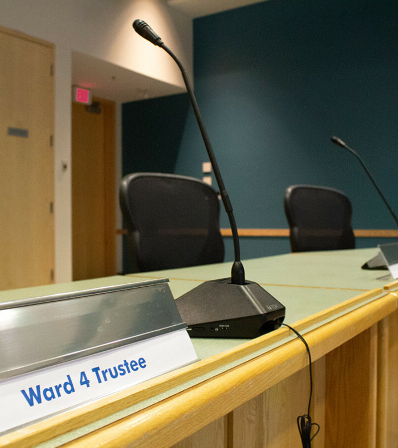 A meeting table with a microphone and a name plate with blue text reading "Ward 4 Trustee"